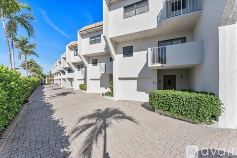 A row of white apartment buildings with balconies and doors are lined up on a paved walkway.