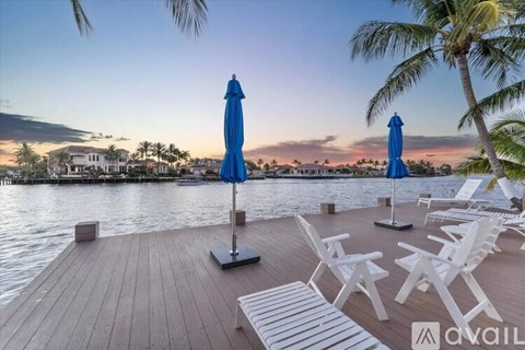A wooden deck with white chairs and blue umbrellas overlooking a body of water.