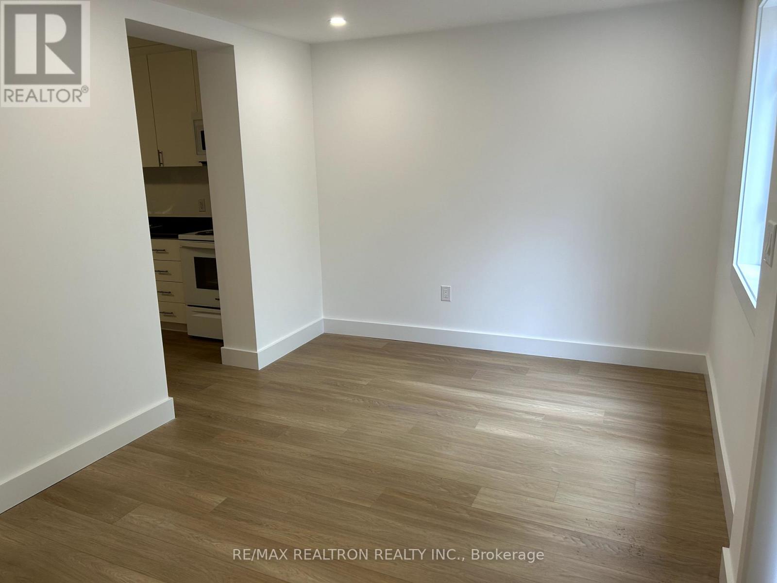 A room with wooden flooring and white walls, with a doorway leading to another room.