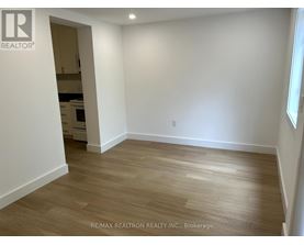 A room with wooden flooring and white walls, with a doorway leading to another room.