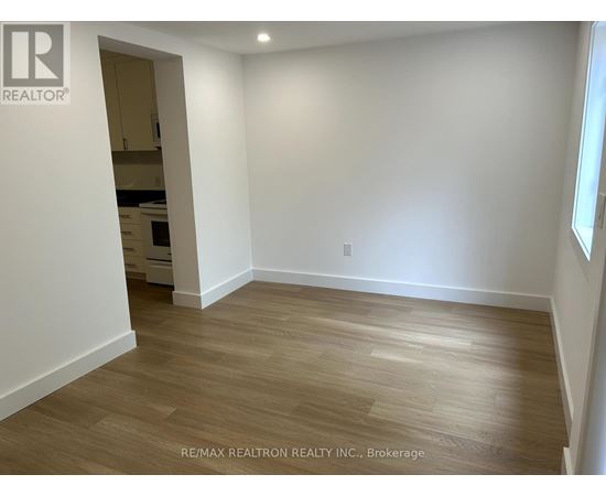 A room with wooden flooring and white walls, with a doorway leading to another room.