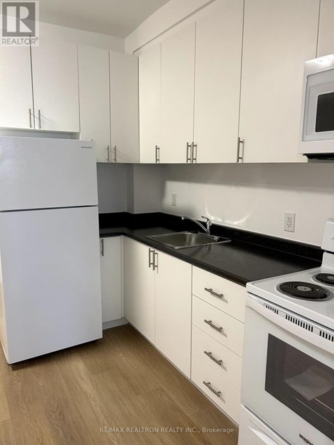 A white refrigerator stands in a kitchen with white cabinets and a black countertop.