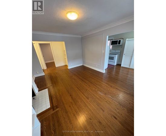 A room with wooden floors and white walls, with a doorway leading to another room.