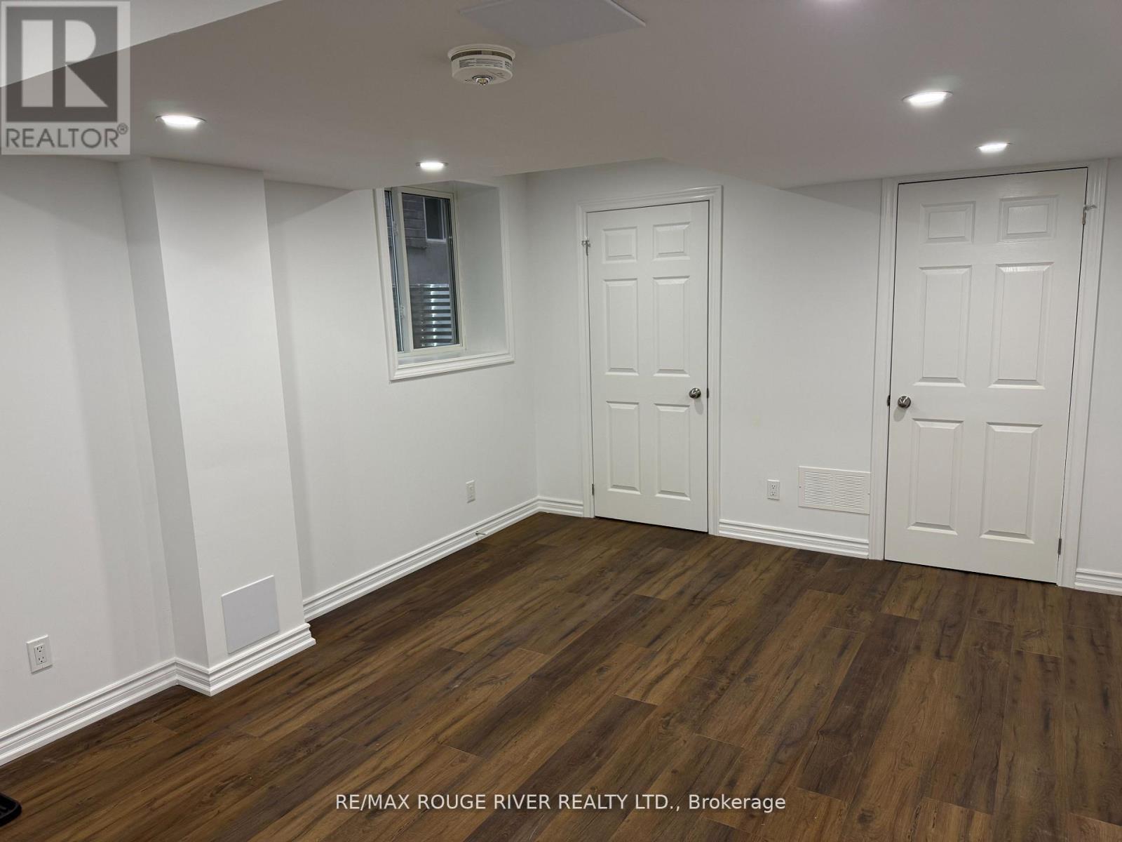 A room with white walls and wooden flooring, with a window and two doors.