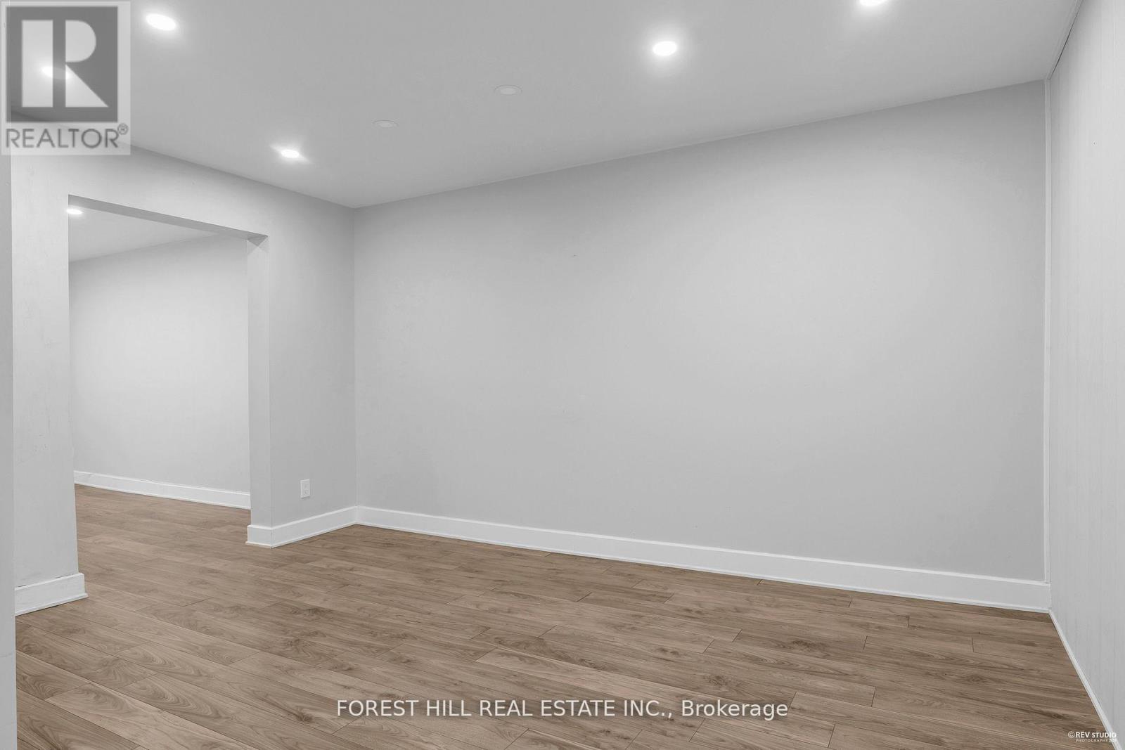 A room with wooden flooring and white walls, with a logo for REALTOR in the top left corner.