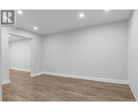 A room with wooden flooring and white walls, with a logo for REALTOR in the top left corner.