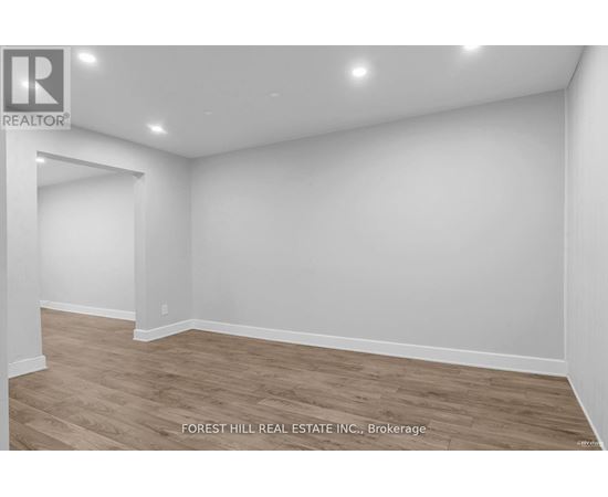 A room with wooden flooring and white walls, with a logo for REALTOR in the top left corner.
