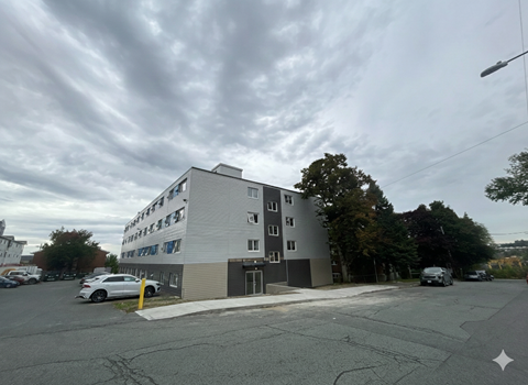 A street view of a multi-story building with cars parked in front.