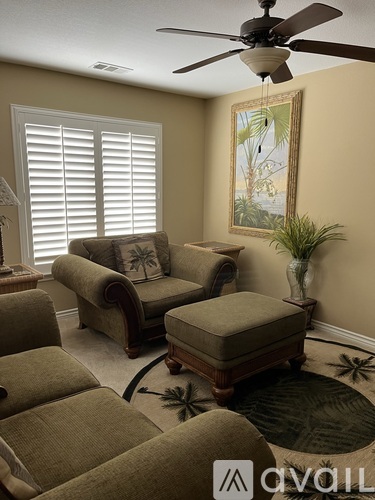 A living room with a brown couch, a chair, and a fan.
