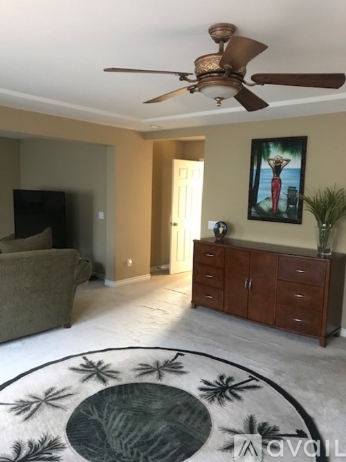 A living room with a ceiling fan and a painting of a woman in red.