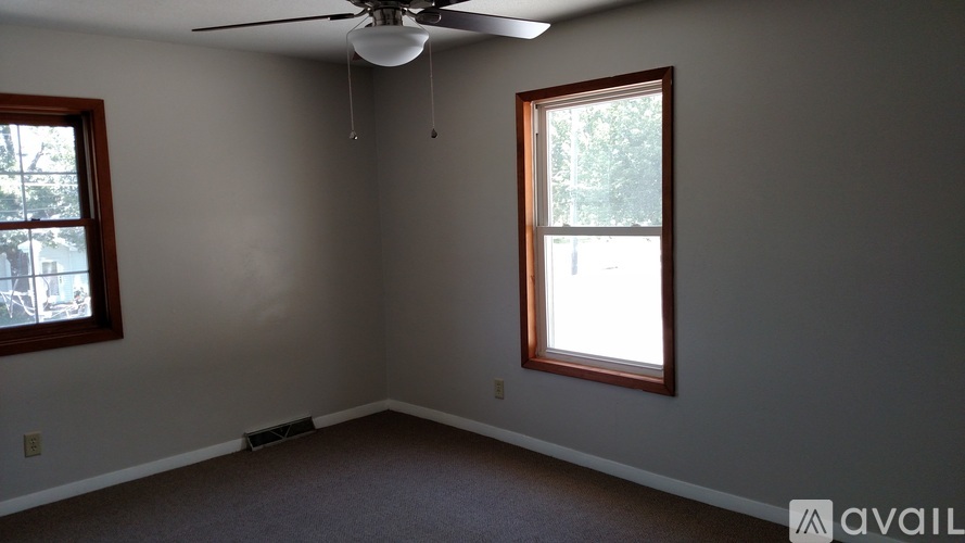 A room with a ceiling fan and two windows.
