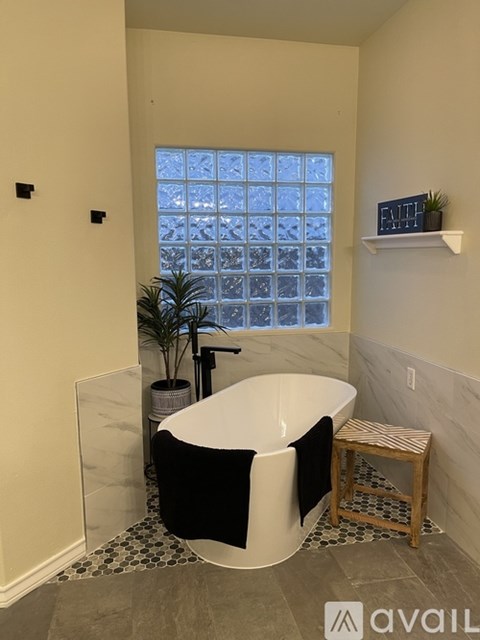 A bathroom with a black and white bathtub, a potted plant, and a window with a view of a building.