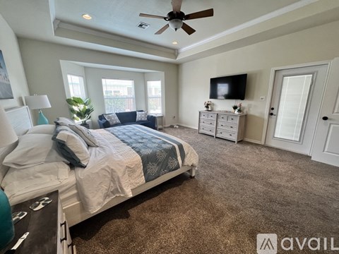 A bedroom with a large bed, a ceiling fan, and a flat-screen TV mounted on the wall.