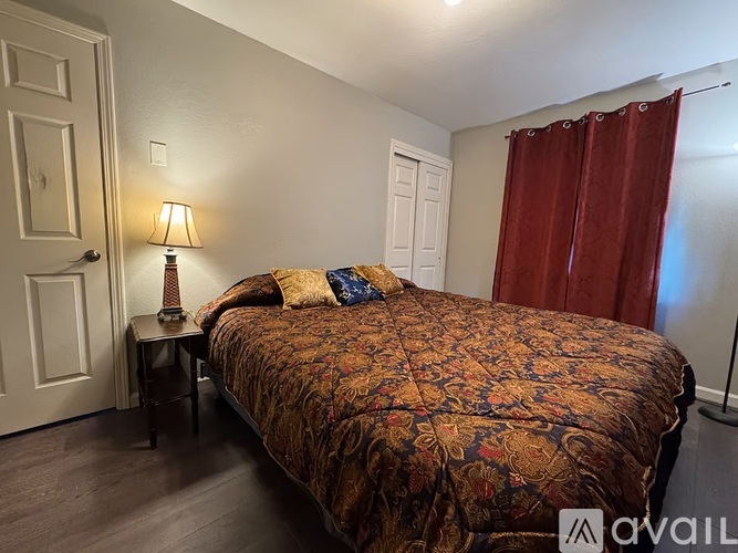 A bedroom with a bed, a lamp, and a window with red curtains.
