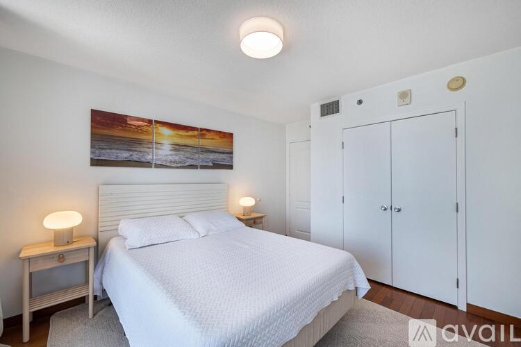 A bedroom with a bed, a nightstand with a lamp, and a painting on the wall.