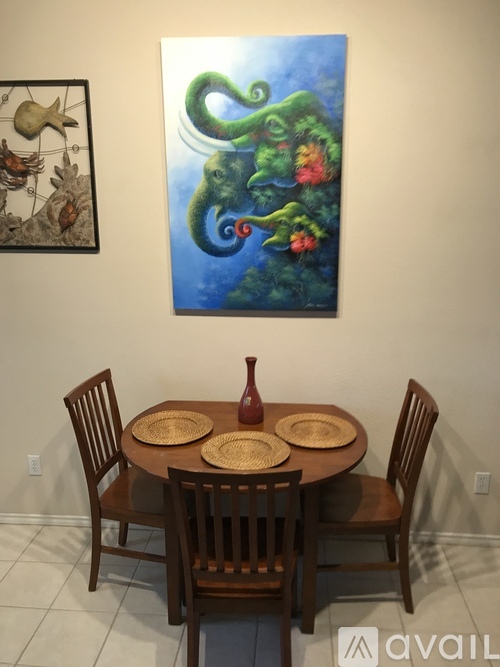 A painting of a green snake with red flowers is hanging on the wall above a wooden dining table with chairs.