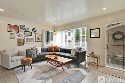 A living room with a grey couch, a wooden coffee table, and a rug with a pattern of squares and rectangles.