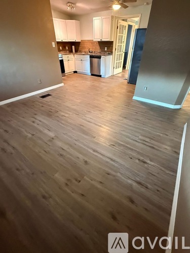 A room with wooden flooring and a kitchen in the background.