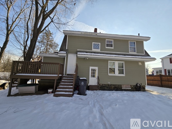 A house with a grey siding and a white door is surrounded by snow.