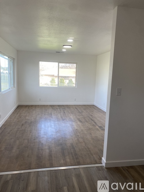 A room with wooden flooring and a window showing a view of trees and a fence.