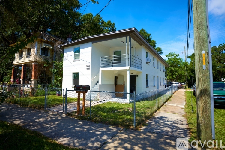 A white two-story house with a balcony on the second floor is in front of a tree.