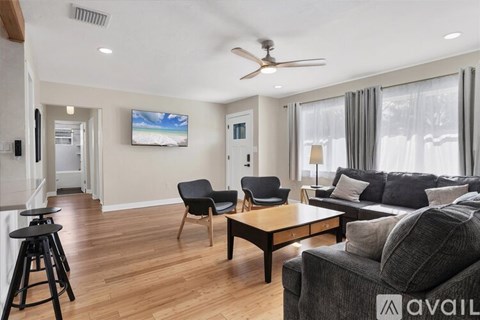 A living room with a grey couch, a black chair, a wooden table, and a television mounted on the wall.