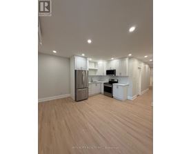 A well-lit, empty kitchen with white cabinets and a wooden floor.