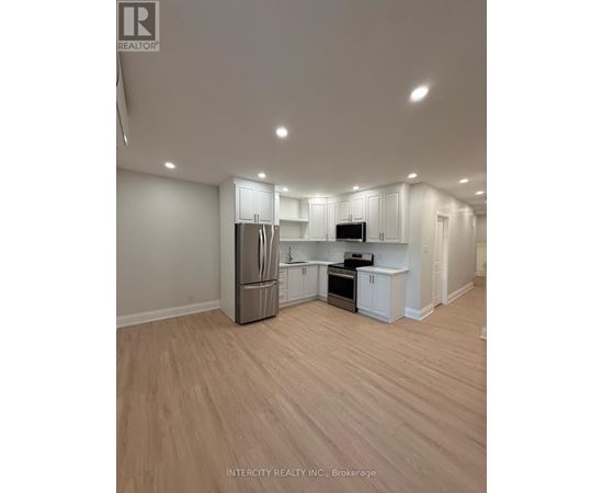 A well-lit, empty kitchen with white cabinets and a wooden floor.
