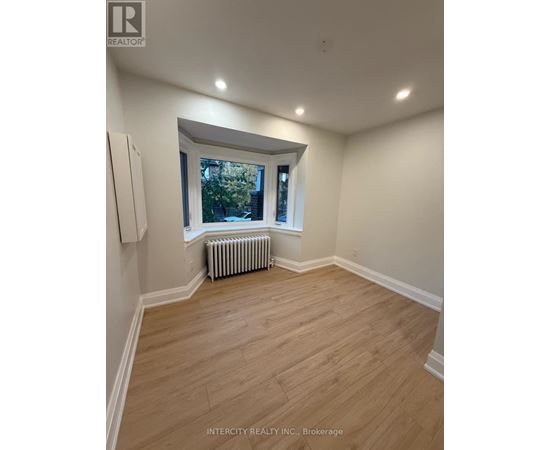 A room with wooden flooring and a window with a view of trees.