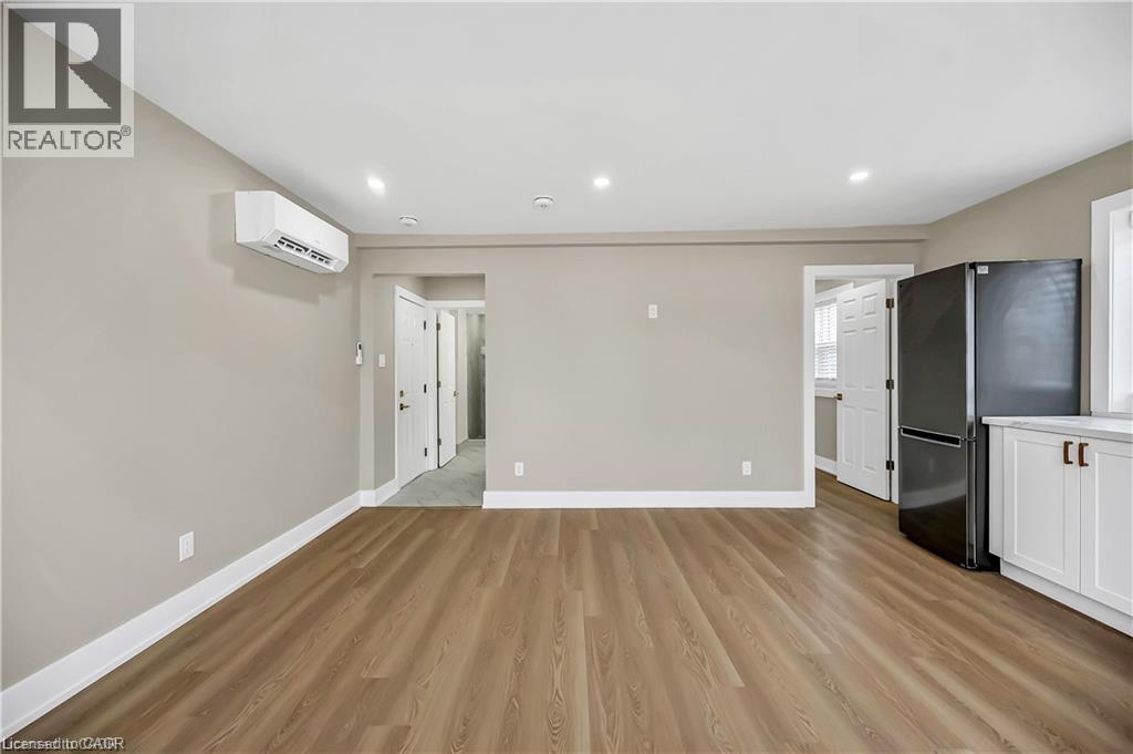 A spacious room with wooden flooring and a kitchen area with white cabinets and appliances.