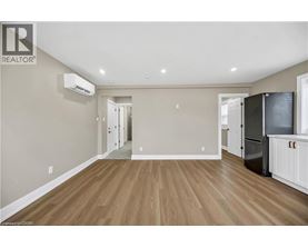 A spacious room with wooden flooring and a kitchen area with white cabinets and appliances.