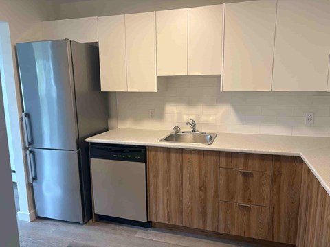 A kitchen with a stainless steel refrigerator, a white countertop, and wooden cabinets.
