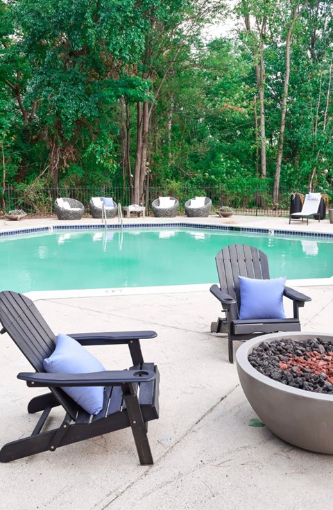 A pool surrounded by trees and chairs.