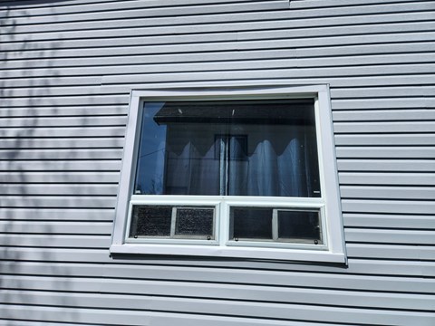 A window with a white frame and black curtains on a house with white siding.