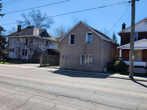 A house with a brown roof and a grey siding is situated on a street with a no parking sign.