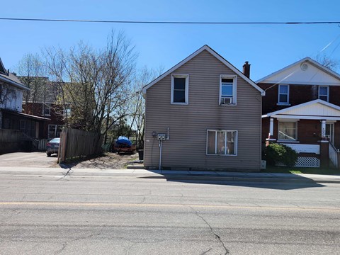 A house with a grey siding and a brown roof is situated on a street.