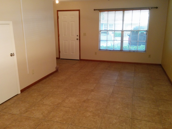 A room with a brown tile floor and a window with blinds.
