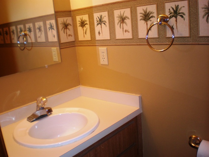 A bathroom with a white sink and a mirror with palm tree pictures on it.