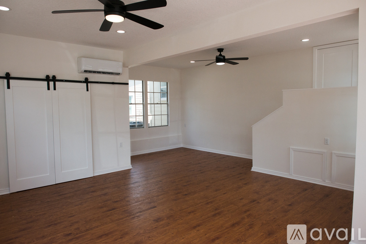 A spacious room with wooden floors and two ceiling fans.