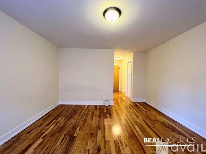 A room with wooden floors and white walls, with a doorway leading to another room.