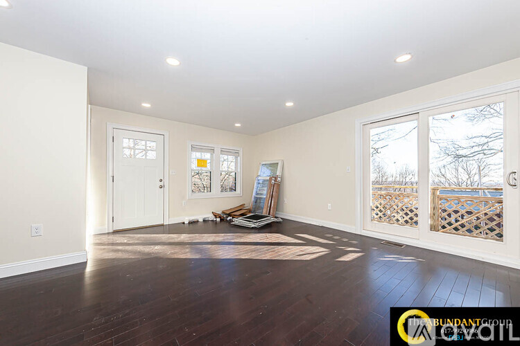 A room with wooden floors and white walls, with a window showing a view of trees and a fence.