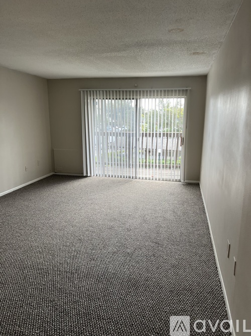 A room with a carpeted floor and a window with blinds.