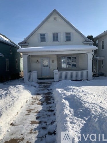 A house with a white porch and a white fence is surrounded by snow.