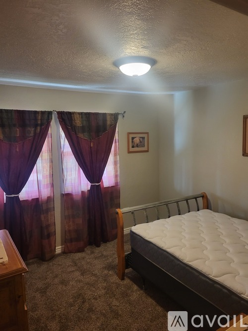 A bedroom with a bed, nightstand, and window with curtains.