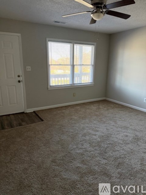 A room with a carpeted floor, a ceiling fan, and a window with blinds.
