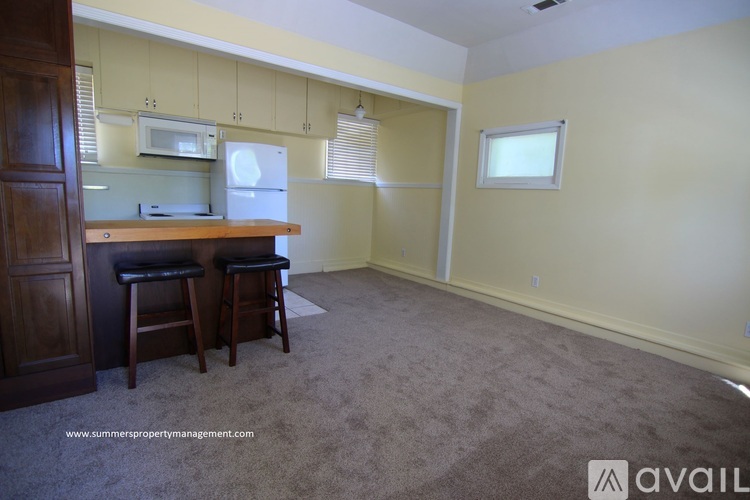 A kitchen with a refrigerator, microwave, and a countertop with two stools.