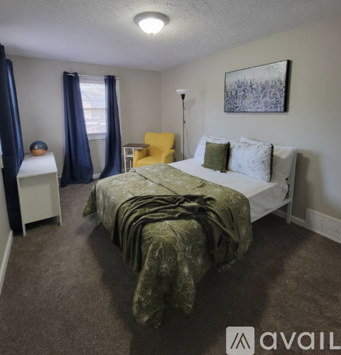 A bedroom with a bed covered in a green blanket and a painting on the wall.