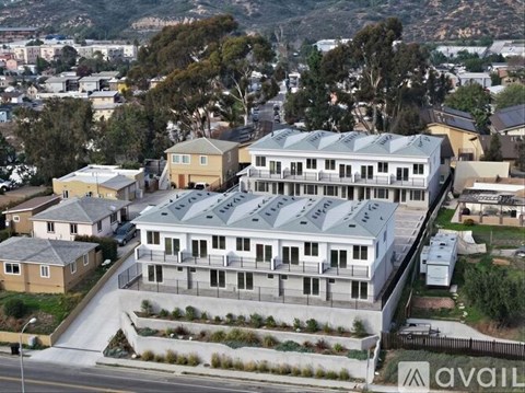 A large building with a grey roof is surrounded by smaller houses.