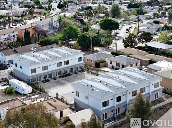A large white building with a row of windows is surrounded by other buildings and trees.