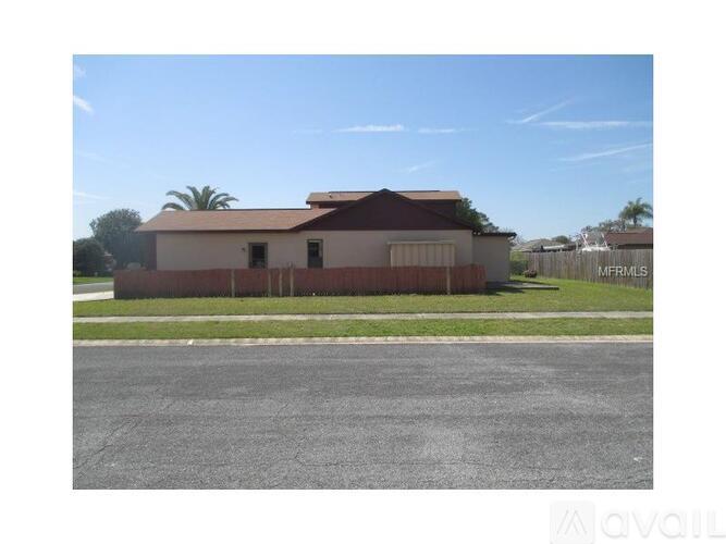 A house with a brown roof and a white wall is in front of a fence.